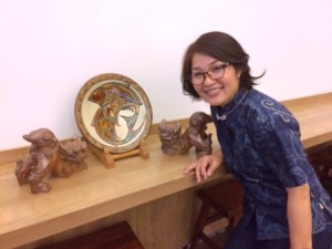 沖縄シーサーの像とポーズを取る恵子さん。着て いるのはかりゆしウエア
